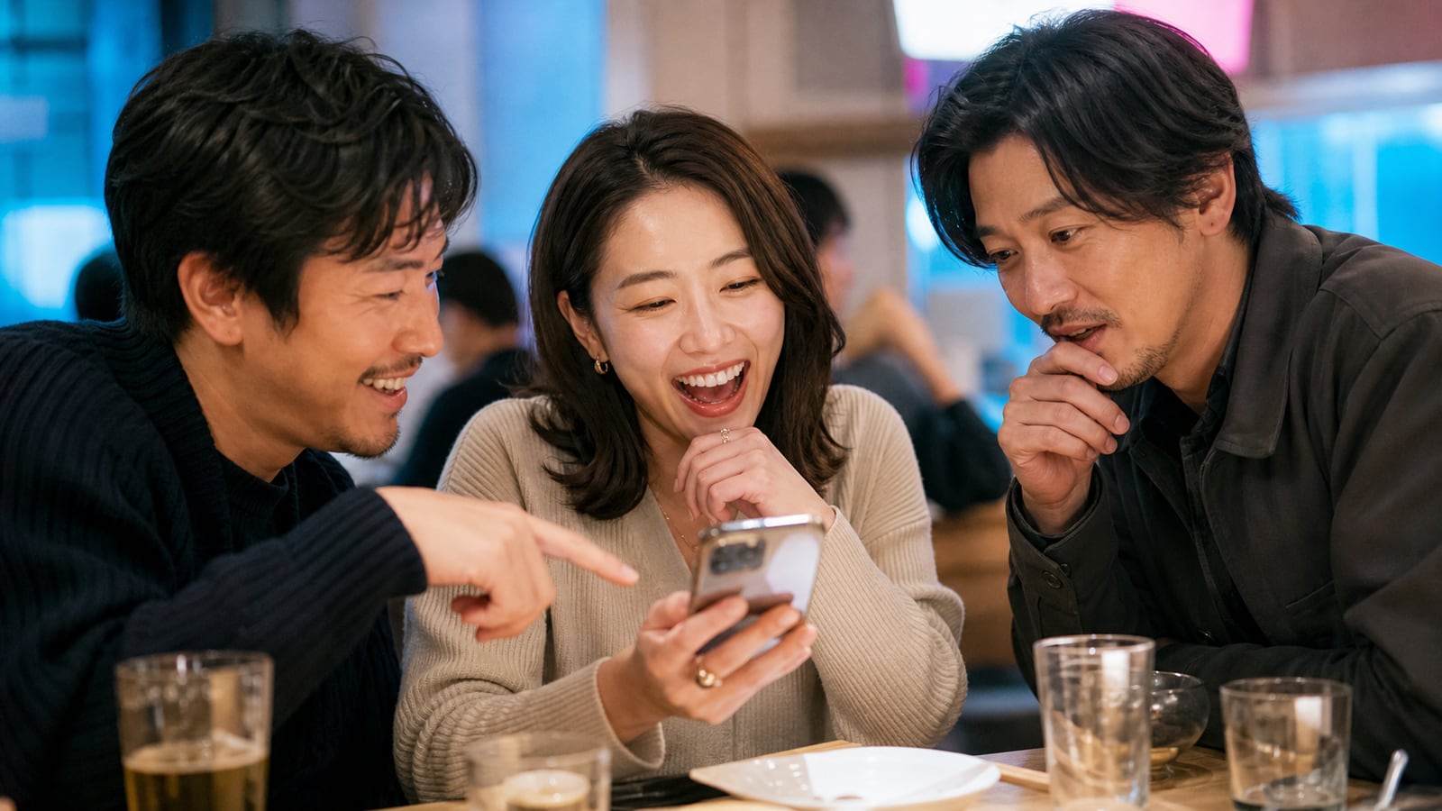 Adult Japanese friends laughing together over a smartphone in a contemporary Tokyo cafe